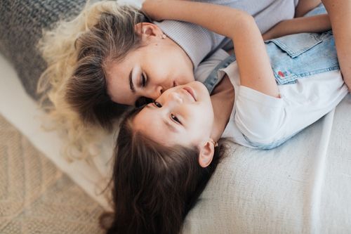 Free A loving mother and daughter share a tender moment lying down indoors, showcasing warmth and togetherness. Stock Photo
