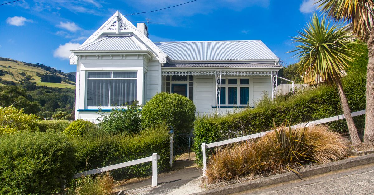 Quaint white detached cottage on a lush hillside under a vibrant blue sky, featuring lush greenery.