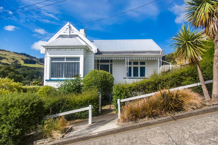 White Cottage House On A Slope And Green Plants