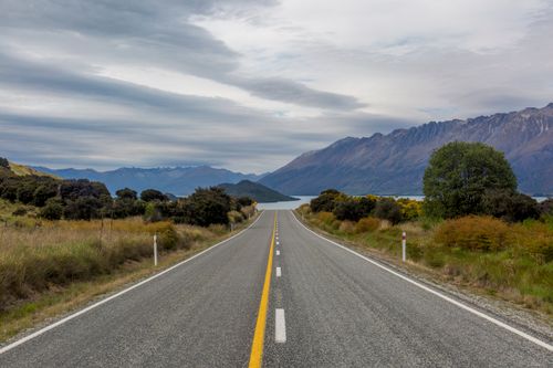 Free Vibrant landscape of a road leading to majestic mountains with an overcast sky. Stock Photo