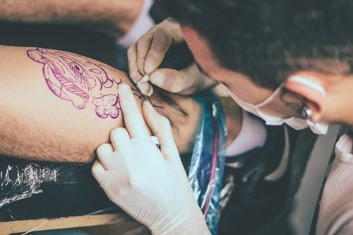 Free Close-up of a tattoo artist creating a detailed design on a client's leg using a needle. Stock Photo