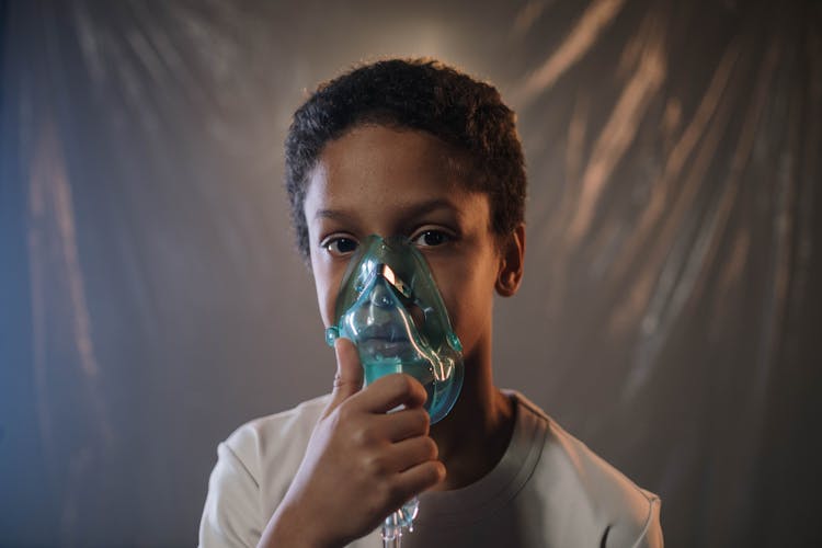 A Boy In White Shirt Holding Green Oxygen Mask