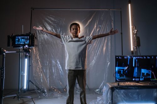 Free A young boy stands with arms outstretched in a professional studio surrounded by equipment. Stock Photo