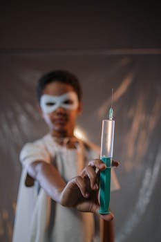 Child dressed as a superhero holding a large syringe, symbolizing bravery.