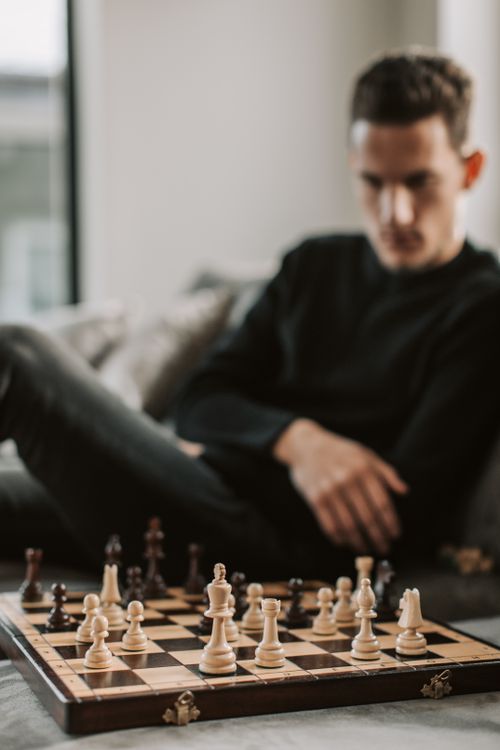 Free Pensive man seated, analyzing a chess game, blurred background for effect. Stock Photo