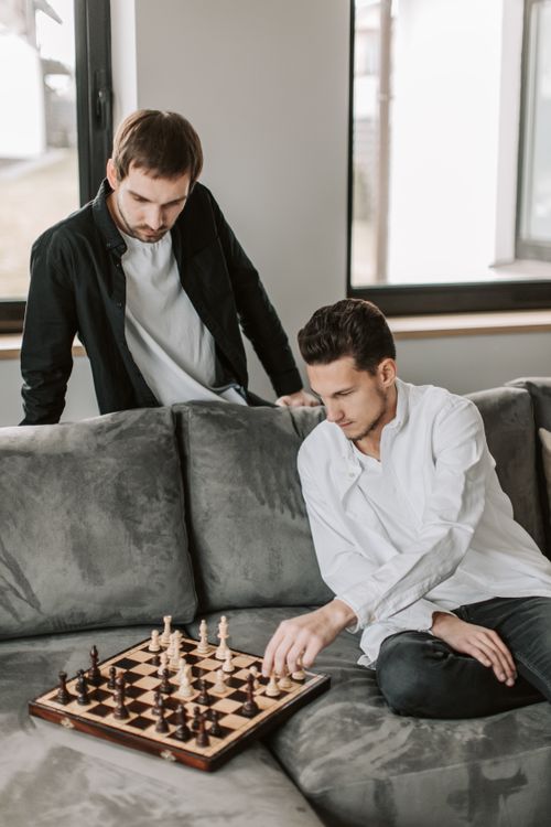 Free Two men engaged in a strategic chess game on a sofa in a modern indoor setting. Stock Photo