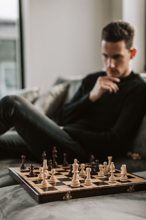 Free Man in black pondering strategy during chess game on a sofa. Stock Photo