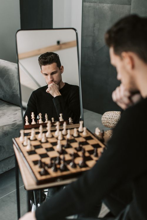 Free A man contemplates move in chess while looking in a mirror, indoors. Stock Photo