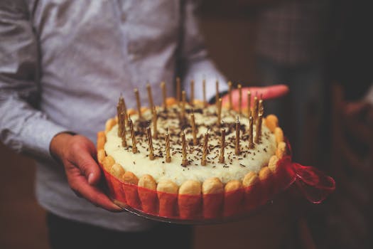 Close-up of a decorated birthday cake with lit candles held by a person at a celebration.