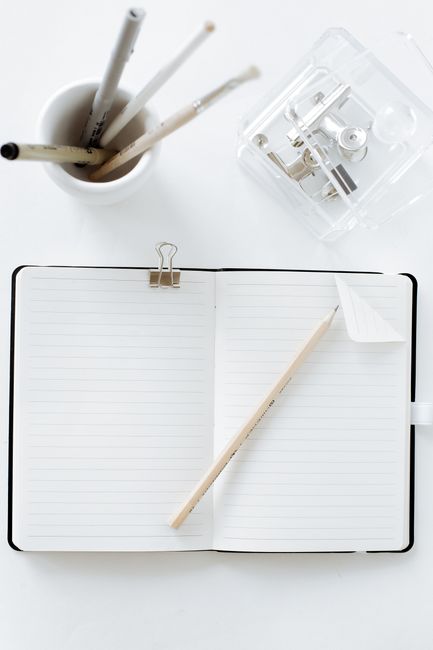 Top view of an open notebook with pen, pencils, and stationery items on a white surface.