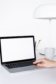 Bright minimalist workspace featuring a blank laptop and white accessories on a desk.