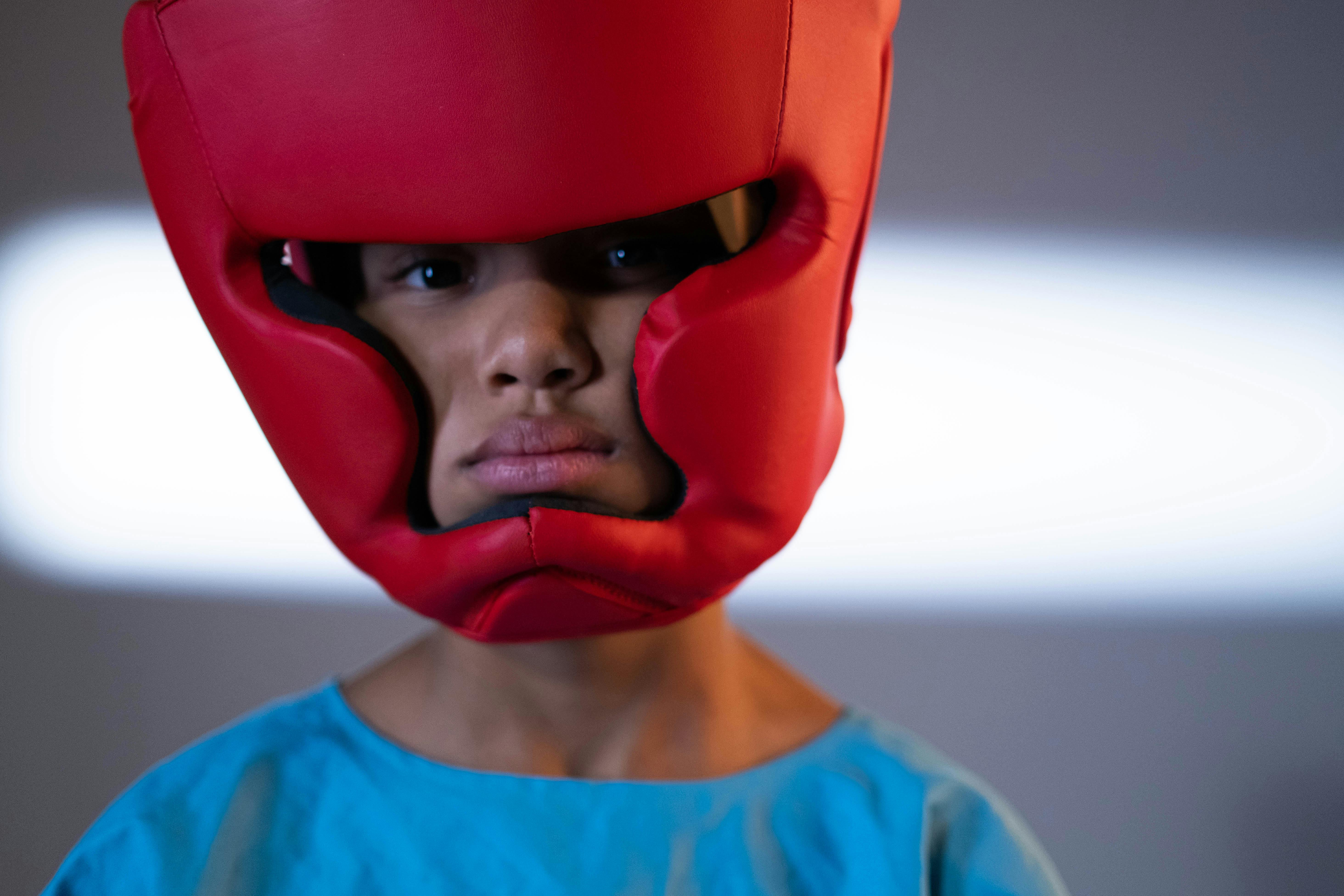 Close-up of a child wearing red protective martial arts headgear, focusing on training and safety.