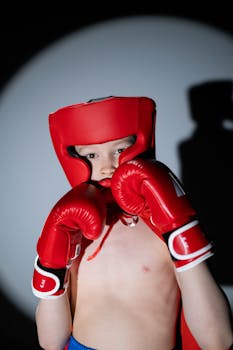 A child wearing red boxing gear poses confidently in a spotlight, embodying youthful determination.