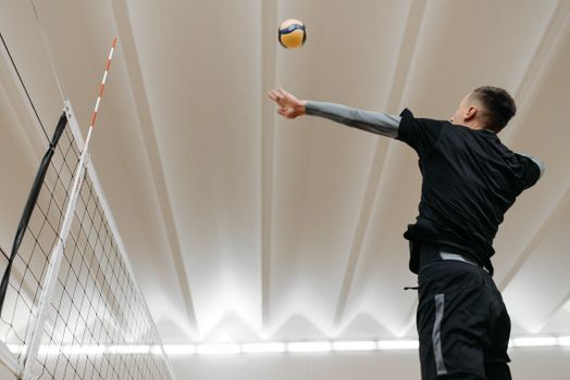 Indoor volleyball player in action, jumping to serve the ball during a game.