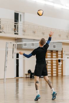 A male athlete practicing a serve in an indoor volleyball court.