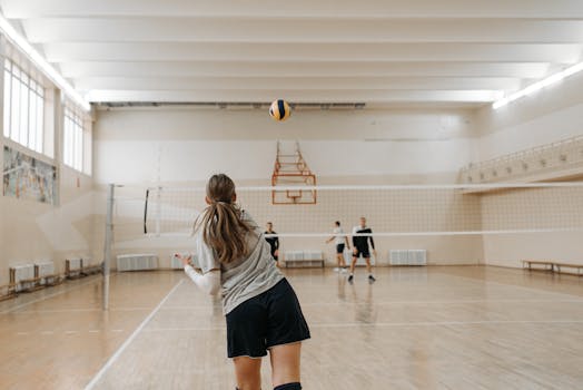 Female athletes practicing volleyball in an indoor gym setting with focus on serve.