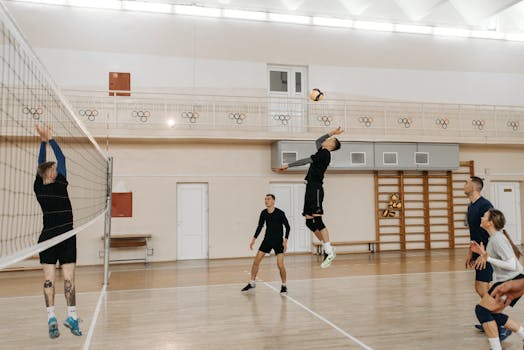 Competitive indoor volleyball match with athletes spiking the ball over the net.