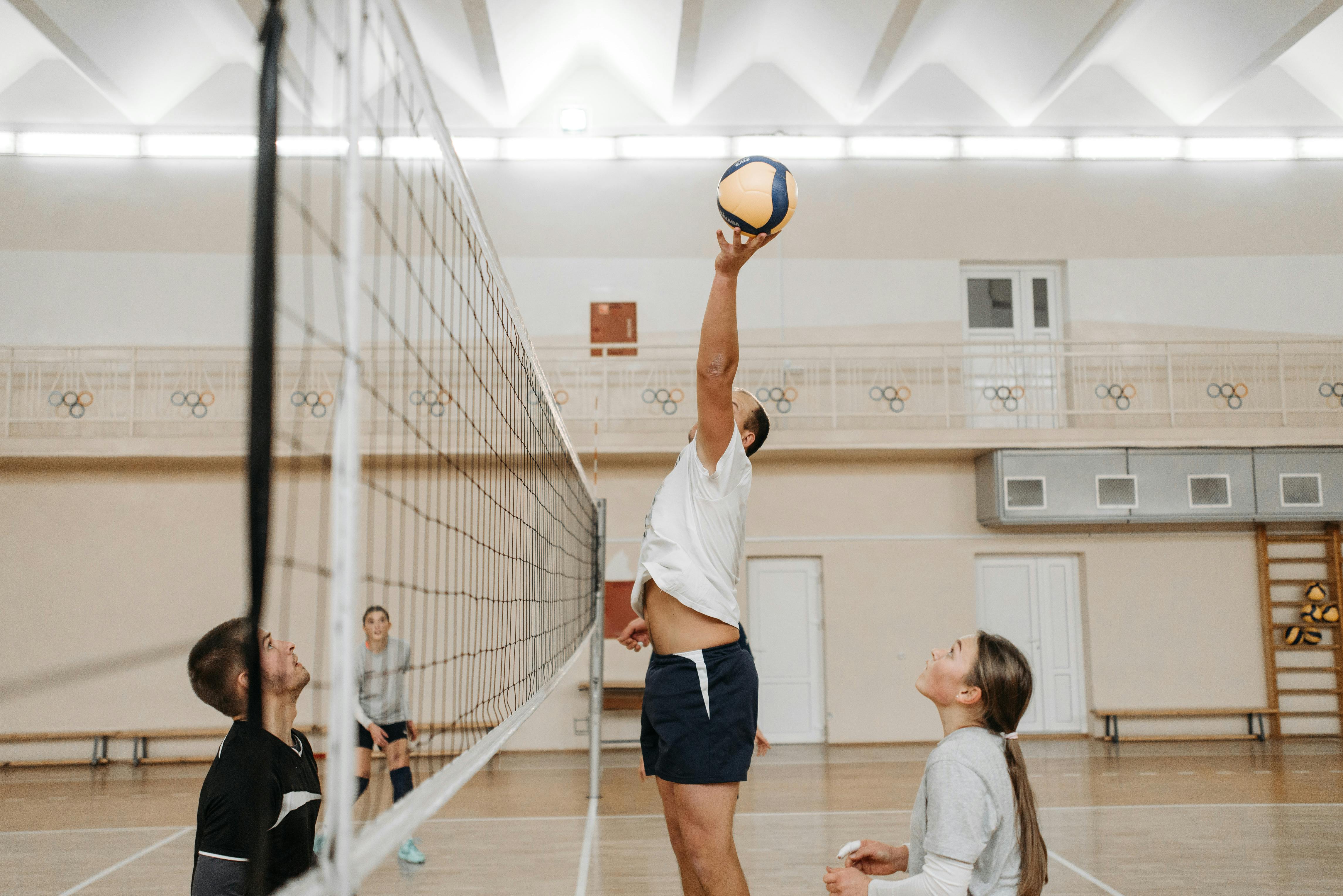 Three players engage in an intense volleyball match inside a sports hall with wooden flooring.