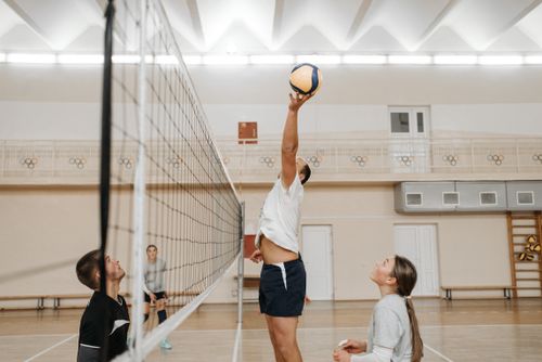 Free Three players engage in an intense volleyball match inside a sports hall with wooden flooring. Stock Photo