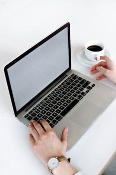A person types on a laptop with a cup of coffee nearby, illustrating a work scenario.
