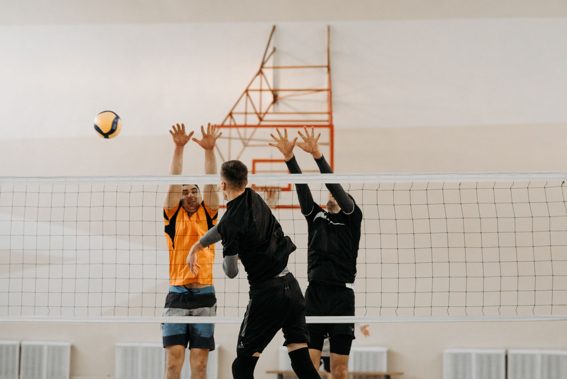 Three athletes competing fiercely in an indoor volleyball match, showcasing a perfect spike block.
