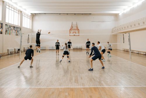 Free Team players engaging in a dynamic indoor volleyball match on a wooden court. Stock Photo