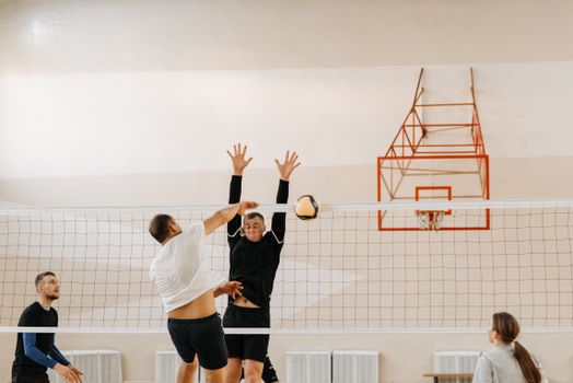 Dynamic volleyball match indoors with players intensely competing, jumping by the net.