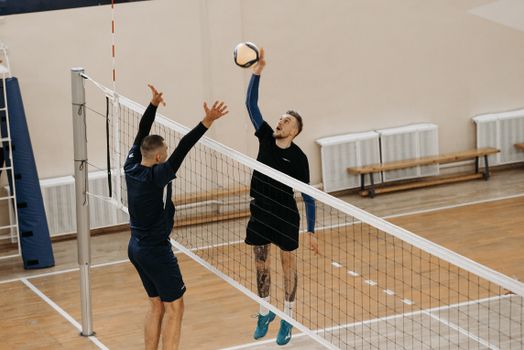 Two male athletes playing a competitive volleyball game indoors.