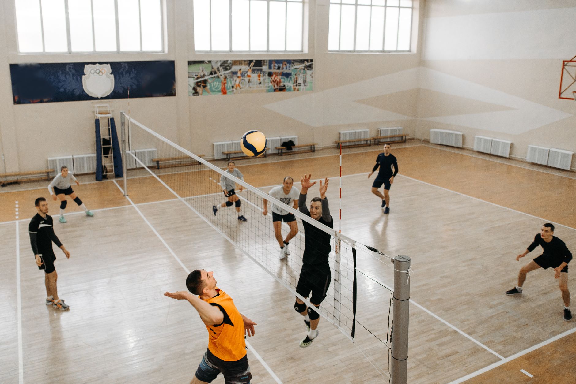 High-energy moment captured during an indoor volleyball game with players mid-action on the court.
