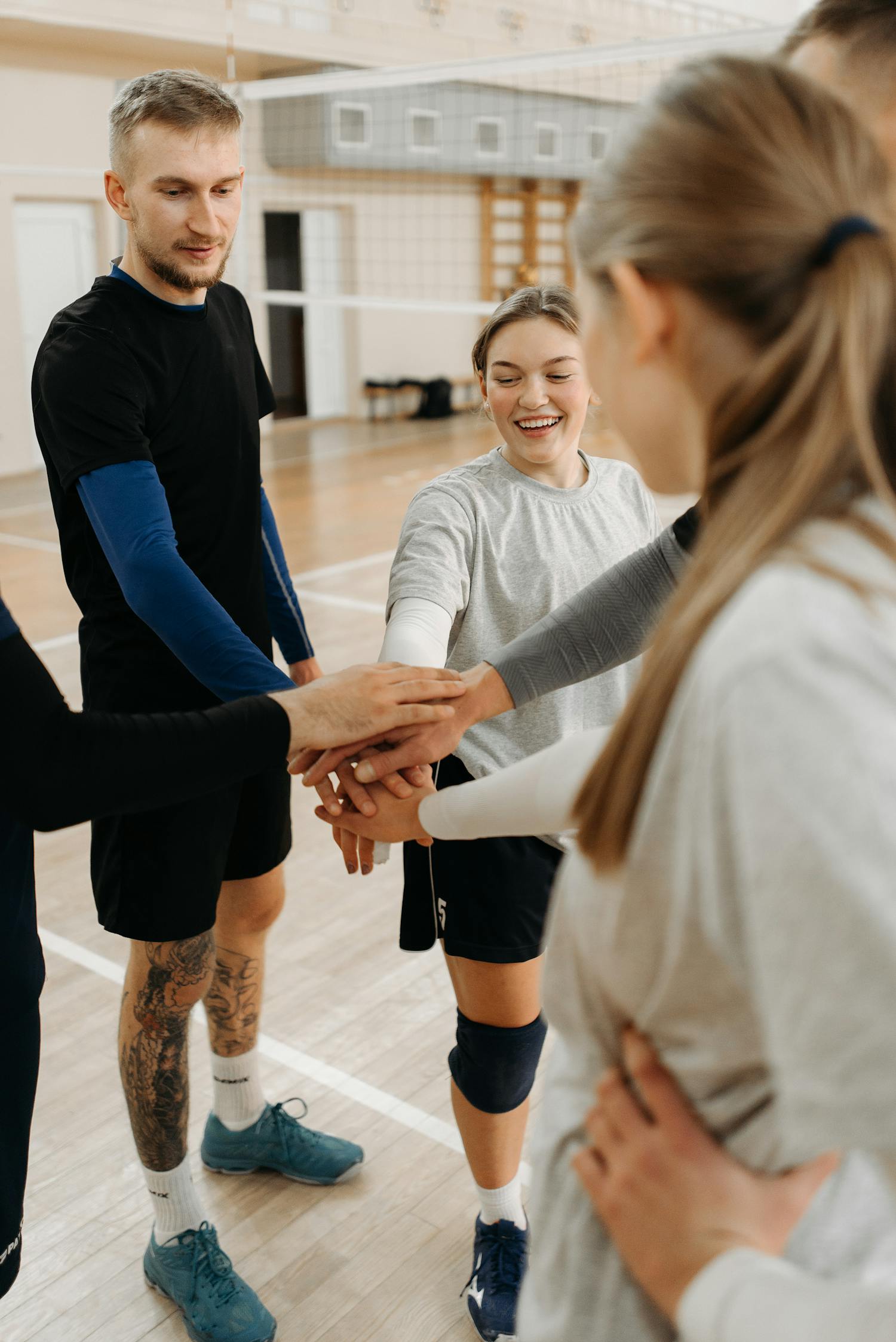 Group of young athletes joining hands in a gym, symbolizing teamwork and unity.