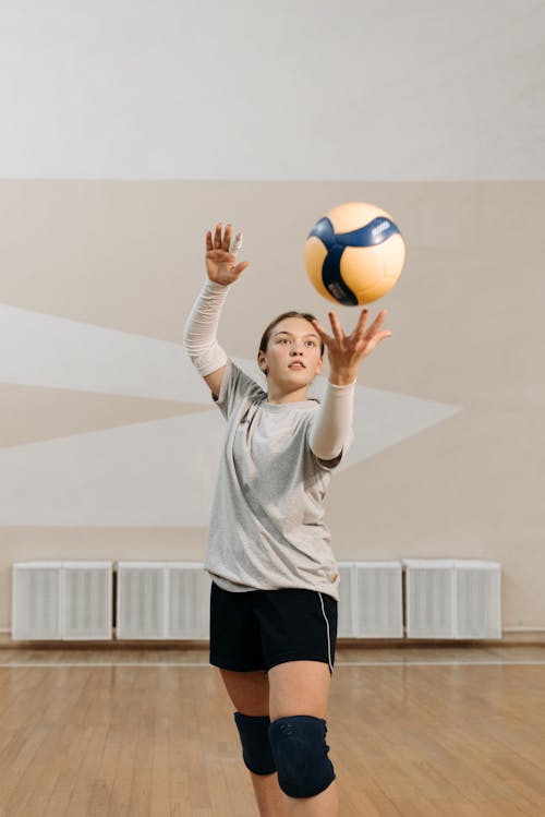 Photo of a Woman in a Gray Shirt Serving a Volleyball
