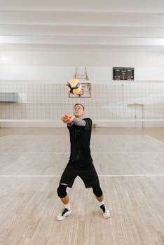 Man practicing volleyball indoors, preparing to hit ball midair.