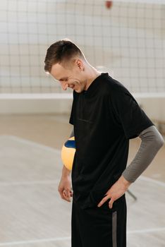 Smiling male volleyball player stands on an indoor court holding a ball, embodying joy and sportsmanship.