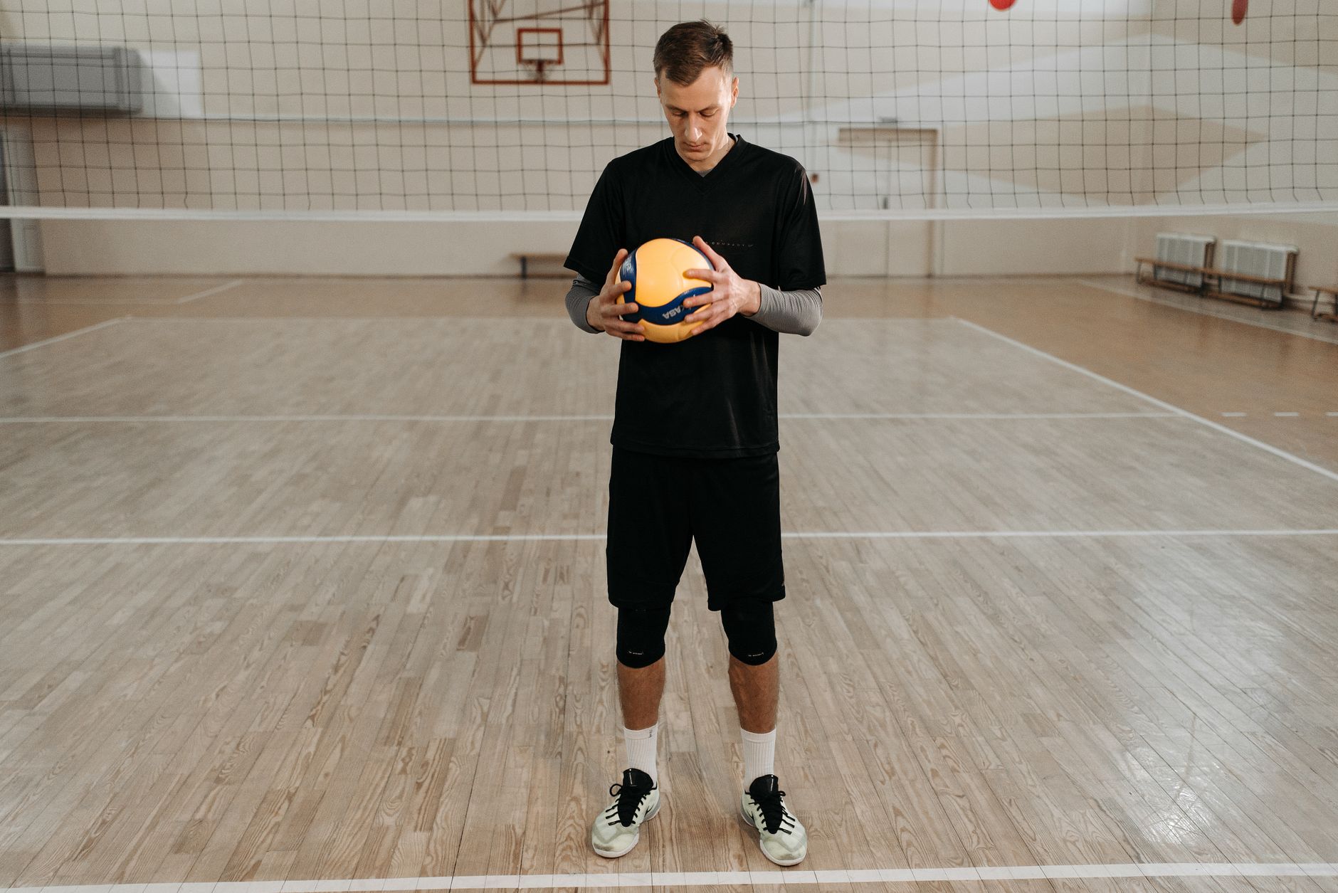 Volleyball player in black attire standing on an indoor court, holding a volleyball.