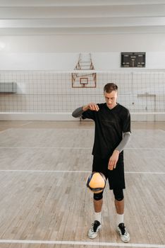 A young man in athletic wear practices volleyball in an indoor gym setting.