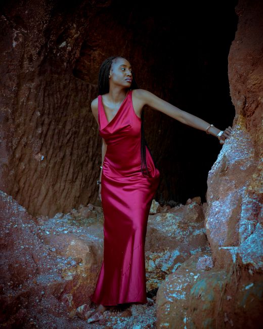 A beautiful black woman in a red dress posing in a rocky outdoor scene.