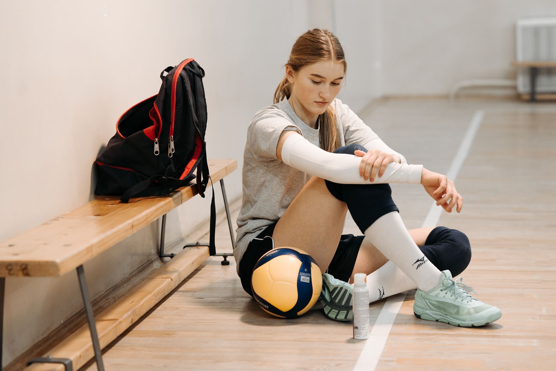 Une joueuse de volley-ball en tenue de sport, assise sur un banc de court intérieur avec de l'équipement.