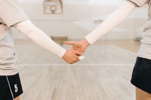 Close-up of athletes holding hands on indoor volleyball court, symbolizing teamwork.