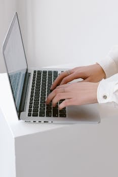 Close-up of hands typing on a laptop in a bright, minimalist indoor setting.