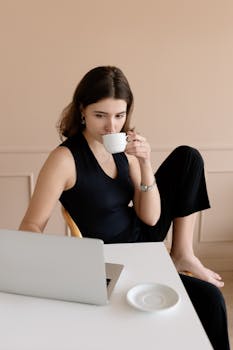A young woman relaxes while working remotely, savoring coffee at home.