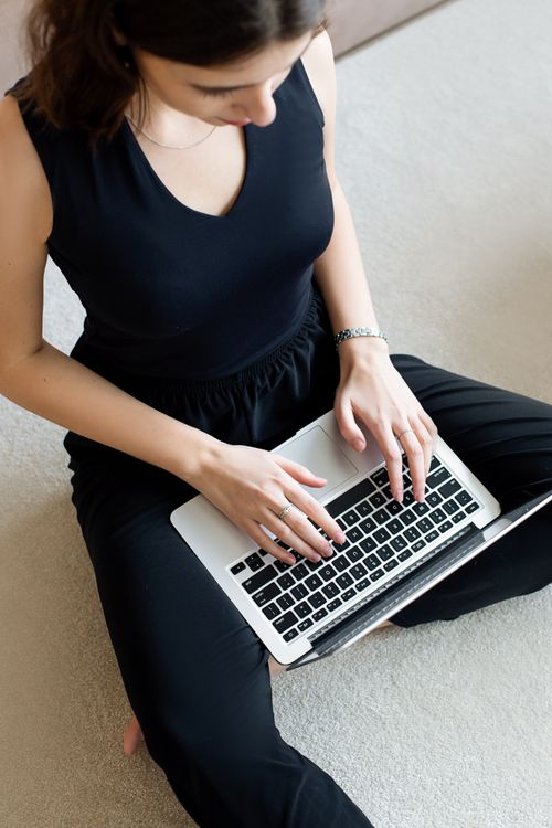 Free Young woman in black outfit working on a laptop from home, showcasing remote work lifestyle. Stock Photo