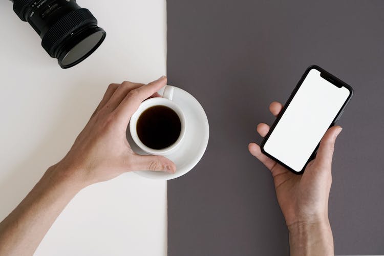 Person Holding White Ceramic Mug And A Smartphone