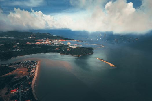 Aerial view of picturesque scenery of calm sea near island with coastal town and beach under cloudy blue sky