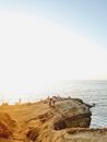 Distant unrecognizable people on rough high cliff washed by rippling sea against cloudless sky and horizon line in sunny day