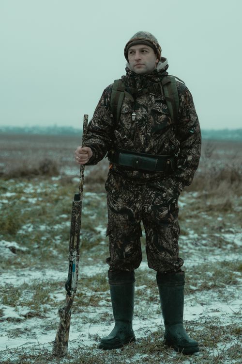 Free Man in camouflage holding a rifle in a snowy field, showcasing hunting attire and preparedness. Stock Photo