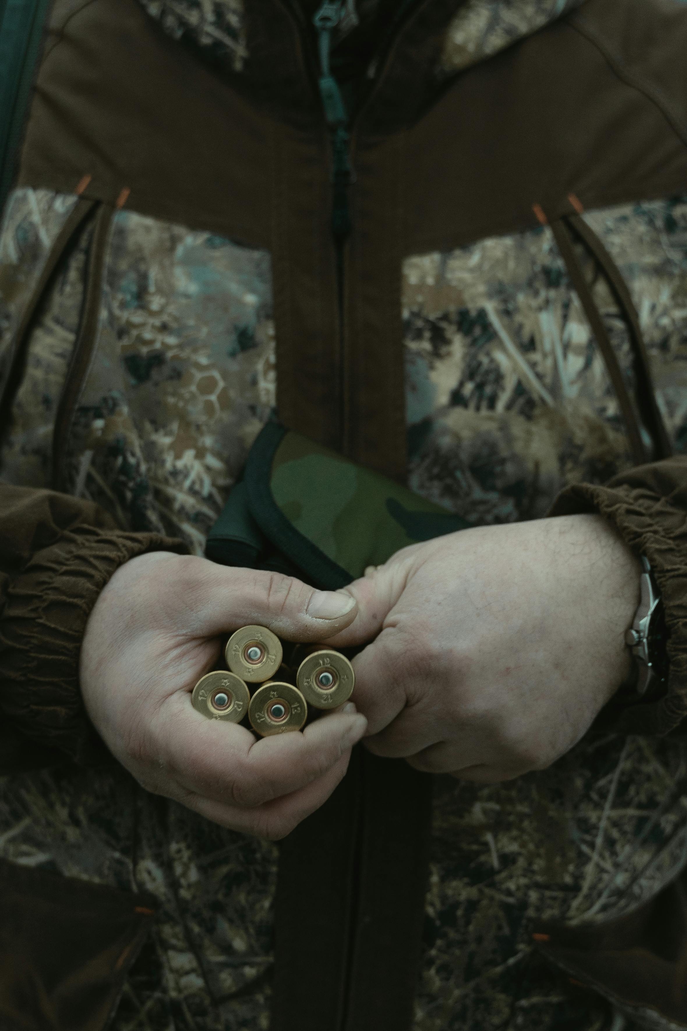 Close-up of a hunter in camouflage holding bullets in hand outdoors.