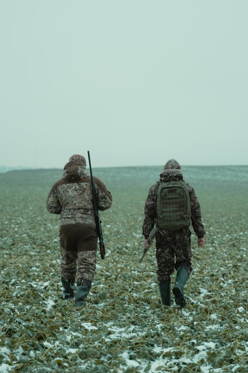 Two men Walking in a Field Holding Rifles