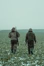 Two men Walking in a Field Holding Rifles