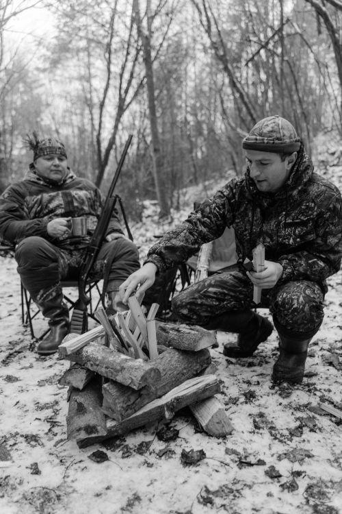 Free Hunters gather around a campfire in a snow-covered forest, preparing for a winter hunt. Stock Photo