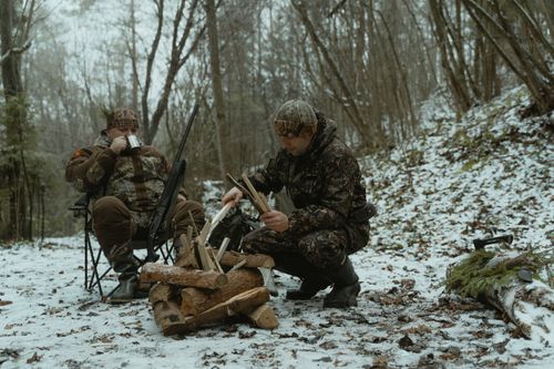 Free Two hunters in camouflage taking a break, building a campfire in snowy woods. Stock Photo